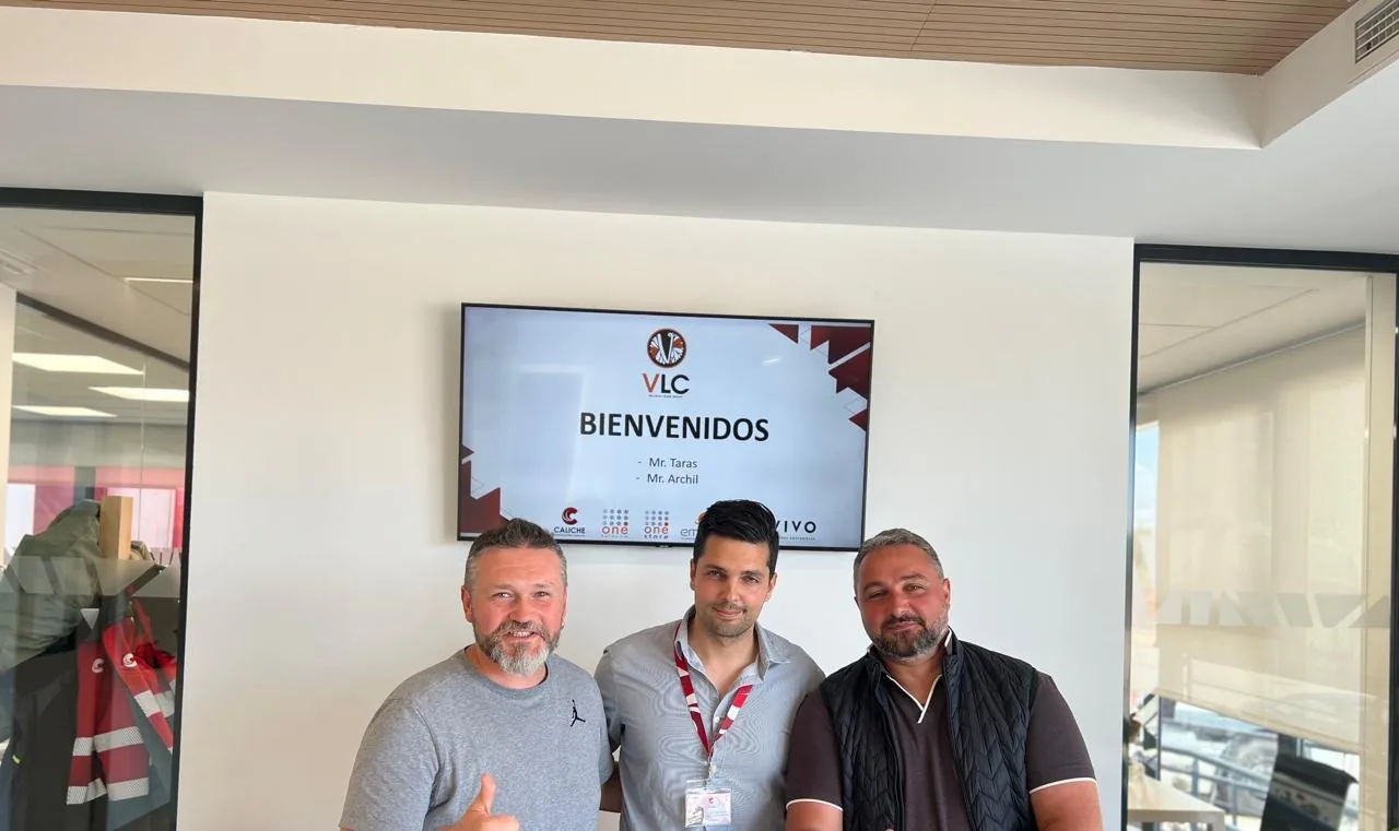 VLC Trade Group staff at a manufacturer visit, a welcome screen behind them reading VLC BIENVENIDOS