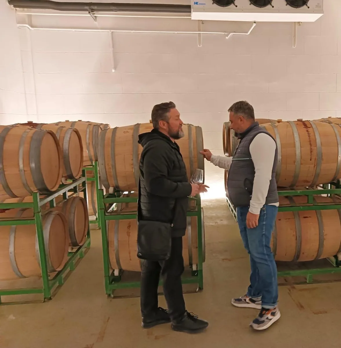 Two men inspecting stacked oak barrels in a Spanish wine cellar